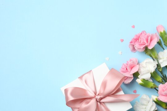 Beautiful bouquet of carnations with gift box on pastel blue background, space for text