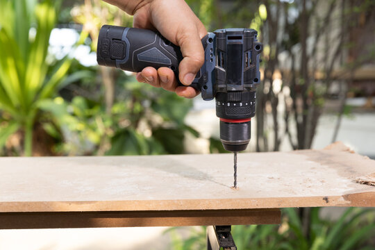 Cordless drill through drilling into rectangular wood piece on workbench