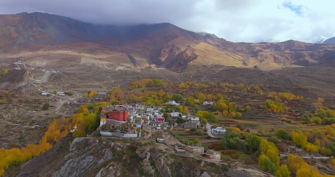 Annapurna Circuit, Mustang, Nepal, Aerial shot of Jharkot village with red monastery and stone buildings, framed by vibrant golden autumn trees and rugged desert mountains.