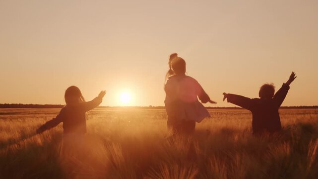 Happy family mother with children running across golden field pretending to be flying airplane at sunset