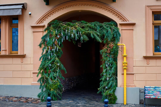 Festive evergreen arch adorned with twinkling lights and ornaments frames the entrance to charming  historic building. Decorated arch with pine branches and glowing lights welcomes visitors