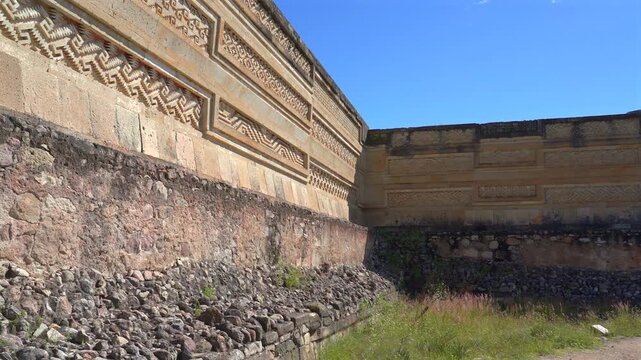 Pan low angle wide shot of ancient Zapotec stone wall with geometric fretwork mosaics at Mitla archaeological site in Oaxaca, Mexico.