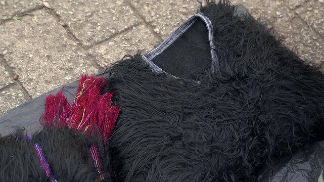 Static close up shot of a traditional black sheepskin wool vest and bright magenta embroidered gloves on display at a market in San Juan Chamula, Chiapas, Mexico.
