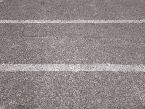 Perspective view of weathered white markings on coarse concrete ground.