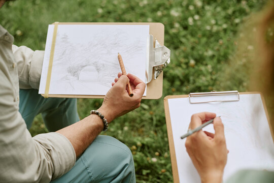 Unrecognizable young adults drawing on clipboards during outdoor art master class, practicing sketching skills. Image suitable for promoting creative workshops and recreational education