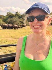 Femme souriante pendant un safari avec un troupeau d'éléphants en arrière-plan © Mathieu