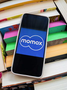 Braunschweig, Germany - August 18, 2026: Box filled with colorful books and modern smartphone displaying momox app logo on screen, concept for selling used books online and decluttering home.