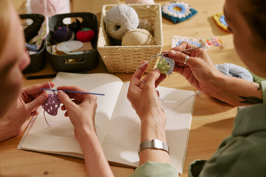 Hands of Caucasian young adult women crocheting colorful yarn squares during creative workshop. Image suitable for promoting craft classes, hobby groups, and DIY tutorials, high angle view