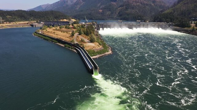 4K aerial drone footage of Bonneville Dam in Columbia River Gorge, Oregon, USA, releasing powerful water through spillways between Oregon & Washington, showcasing hydroelectric power, renewable energy