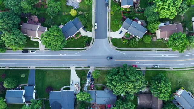 Top-down drone shot sliding over a Fairfax, Virginia T-intersection. Cars drive past single-family homes, driveways, and green summer trees in a quiet neighborhood.