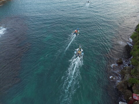 Aerial drone footage of a traditional fishing boat sailing across the vast open ocean. Cinematic aerial perspective capturing the vessel moving through deep blue waters with gentle waves