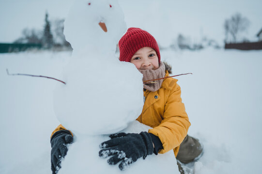 Child in yellow jacket with snowman outside in winter