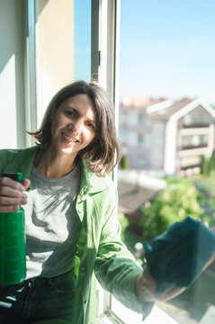 Smiling housekeeper washing window with spray bottle and cloth