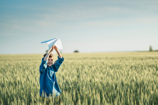 A smiling boy throws a paper airplane in a green field