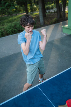 An excited teenage boy celebrates winning table tennis outdoors