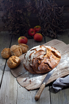 Crusty bread and old bread knife on chopping board, granary rolls