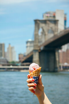 USA, New York, Brooklyn, Close up of woman hand holding a strawberry ice cream cone with Brooklyn Bridge in background