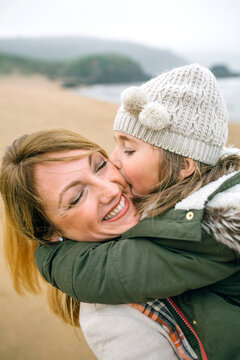 Girl kissing happy mother on the beach in winter