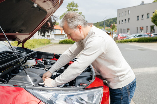Driver checking car engine under open hood outdoors