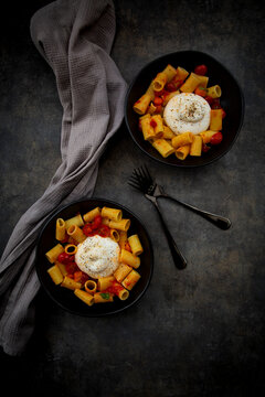 Rigatoni pasta with roasted tomatoes and burrata in a black bowl