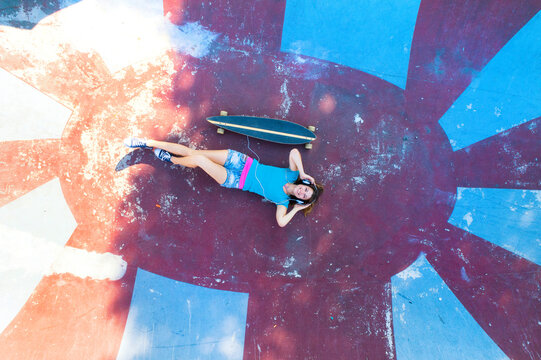 Female longboarder with earphones lying in halfpipe
