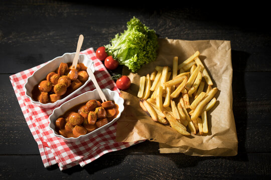 Two bowls of Currywurst and French fries on baking paper