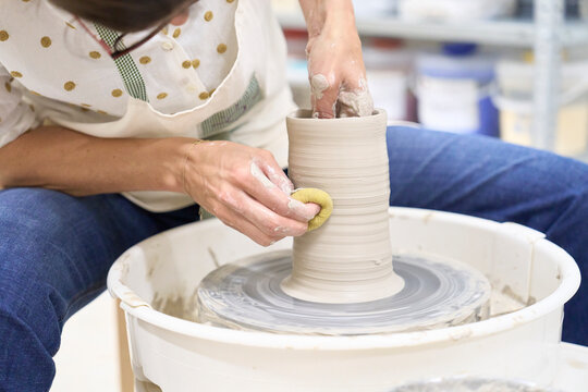 A woman skillfully shapes clay on a pottery wheel indoors