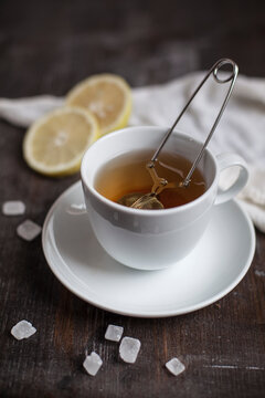 Preparation for tea with tea strainer in cup, slices of lemon, rock sugar on wooden table, studio