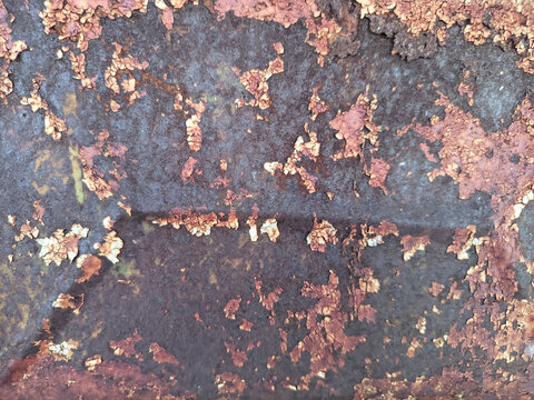 A close-up view of a heavily corroded metal surface featuring cracked, peeling paint and deep rust textures.