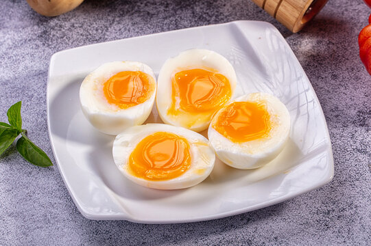 Four soft boiled egg halves with runny yolk on white plate