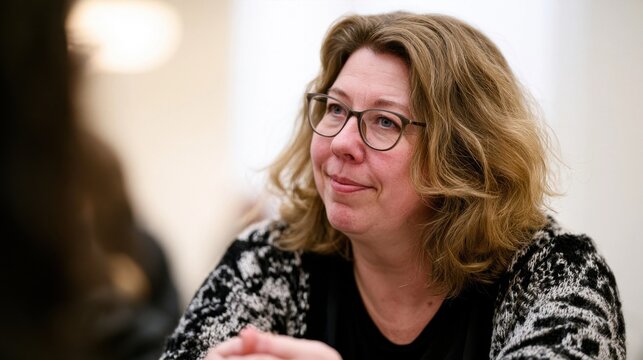 Woman with light brown wavy hair and glasses in a black and white patterned top