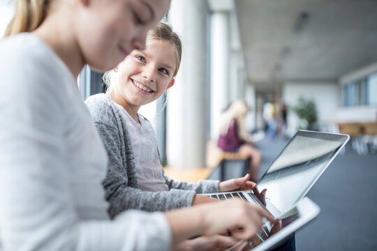 Cheerful schoolgirls using technology to enhance their learning experience while walking down the school corridor