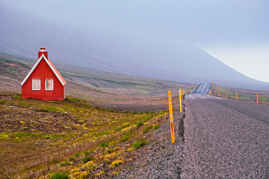 Iceland, Europe: the road along the East Fjords landscape, shrouded in fog, with view of a small, iconic, isolated wooden cottage 
