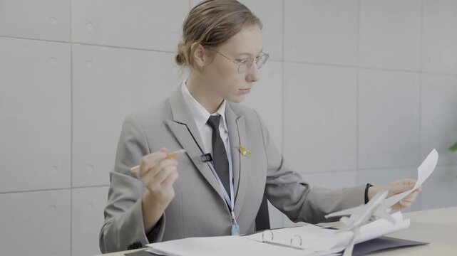 Professional pilot in glasses writing notes while reviewing flight paperwork at her desk in the office.
