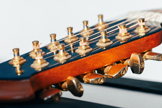 Vintage twelve string guitar headstock displays aged brass tuning pegs and wound strings in sharp detail.  Golden tuning pegs and taut strings of acoustic guitar