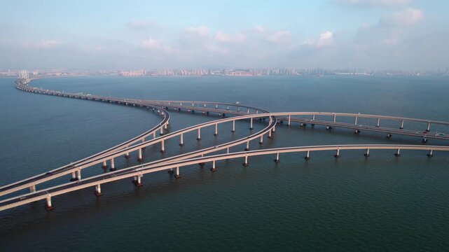 A large multi-level sea bridge interchange spanning over calm blue water, with distant city skyline under clear sky.