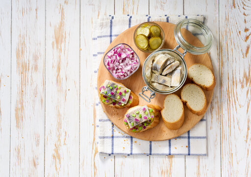 Slices of baguette with pieces marinated herring fillet with with red onions and pickles on table. Top view.