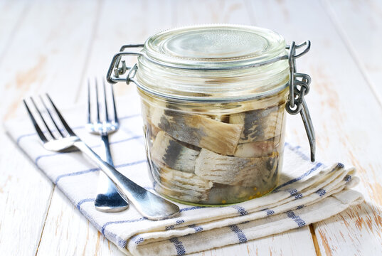 Marinated herring in a jar with herbs on a white table, selective focus. Herring marinated with oil and salt