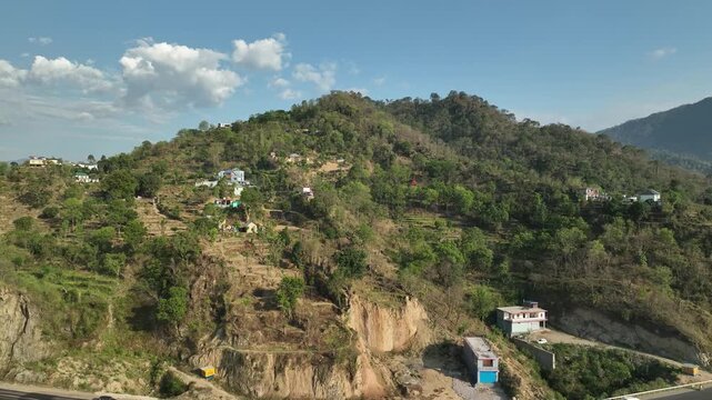 Aerial bird eye view of cars and trucks driving on a Himalayan mountain road below a hillside settlement Lahaul Valley India shot by a drone flying over the highway
