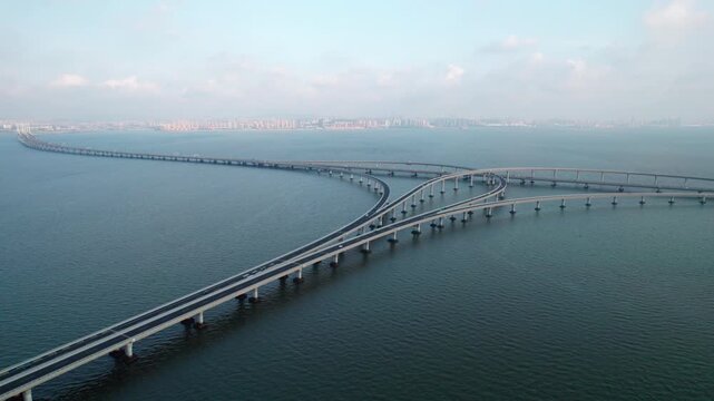 An elevated highway bridge with interchange spans across calm coastal water, connecting distant urban areas.