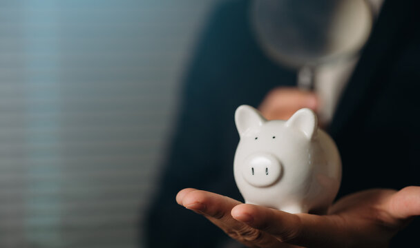 A professional adult in a business suit holding a white piggy bank, symbolizing savings, financial planning, and investment concepts in a modern economic setting.