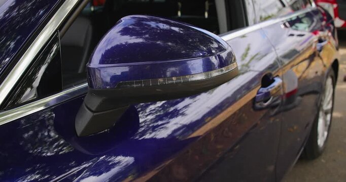 Close up slow motion footage of blue flashing emergency lights integrated into the wing mirror of an unmarked undercover British police car showing discreet equipment fitted to a dark blue vehicle