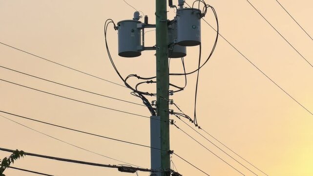 Utility pole electrical transformers silhouette against vibrant orange sunset sun