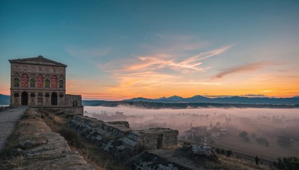 Naklejka premium Historic Building Overlooking Misty Landscape at Sunrise with Colorful Windows