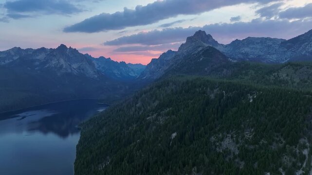 Aerial view of the Sawtooth Mountains and Redfish Lake during a vibrant sunset with pine forests and rocky peaks in Stanley, Idaho, United States.