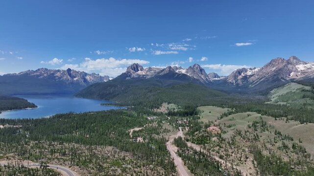 Aerial view of the Sawtooth Mountains and Redfish Lake with surrounding pine forests and a winding road in Stanley, Idaho, United States.