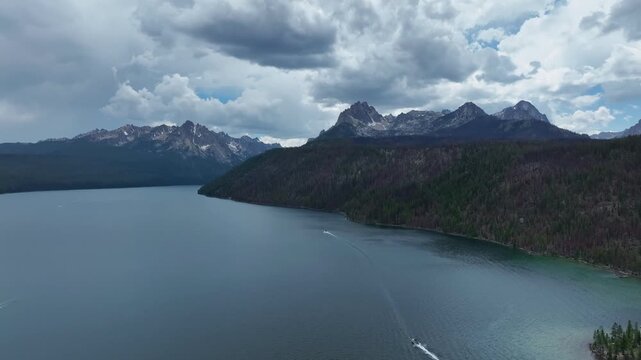 Aerial view of Redfish Lake and the Sawtooth Mountains with dense pine forests and cloudy skies in Stanley, Idaho, United States.