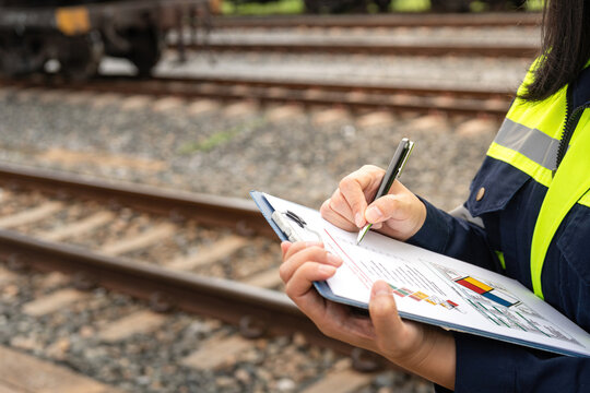 A safety officer is checking on hazardous chemical material checklist for risk assessment before tranportation the dangerous good with train tanker railway background. Industrail working scene.