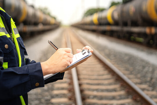 A safety officer is checking on hazardous chemical material checklist for risk assessment before tranportation the dangerous good with train tanker railway background. Industrail working scene.