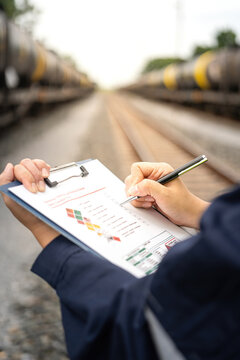 A safety officer is checking on hazardous chemical material checklist for risk assessment before tranportation the dangerous good with train tanker railway background. Industrail working scene.